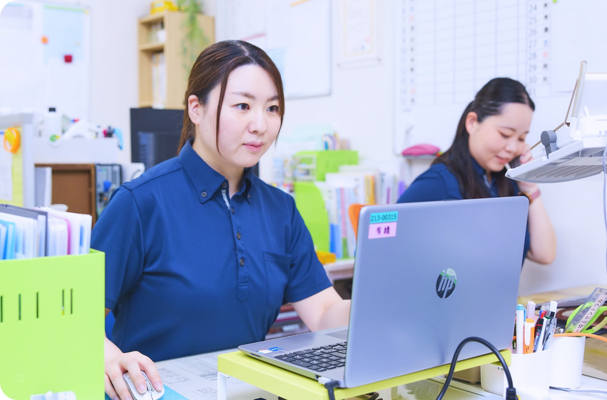 事務室でケアプランを作成する施設ケアマネジャーと電話対応するスタッフ