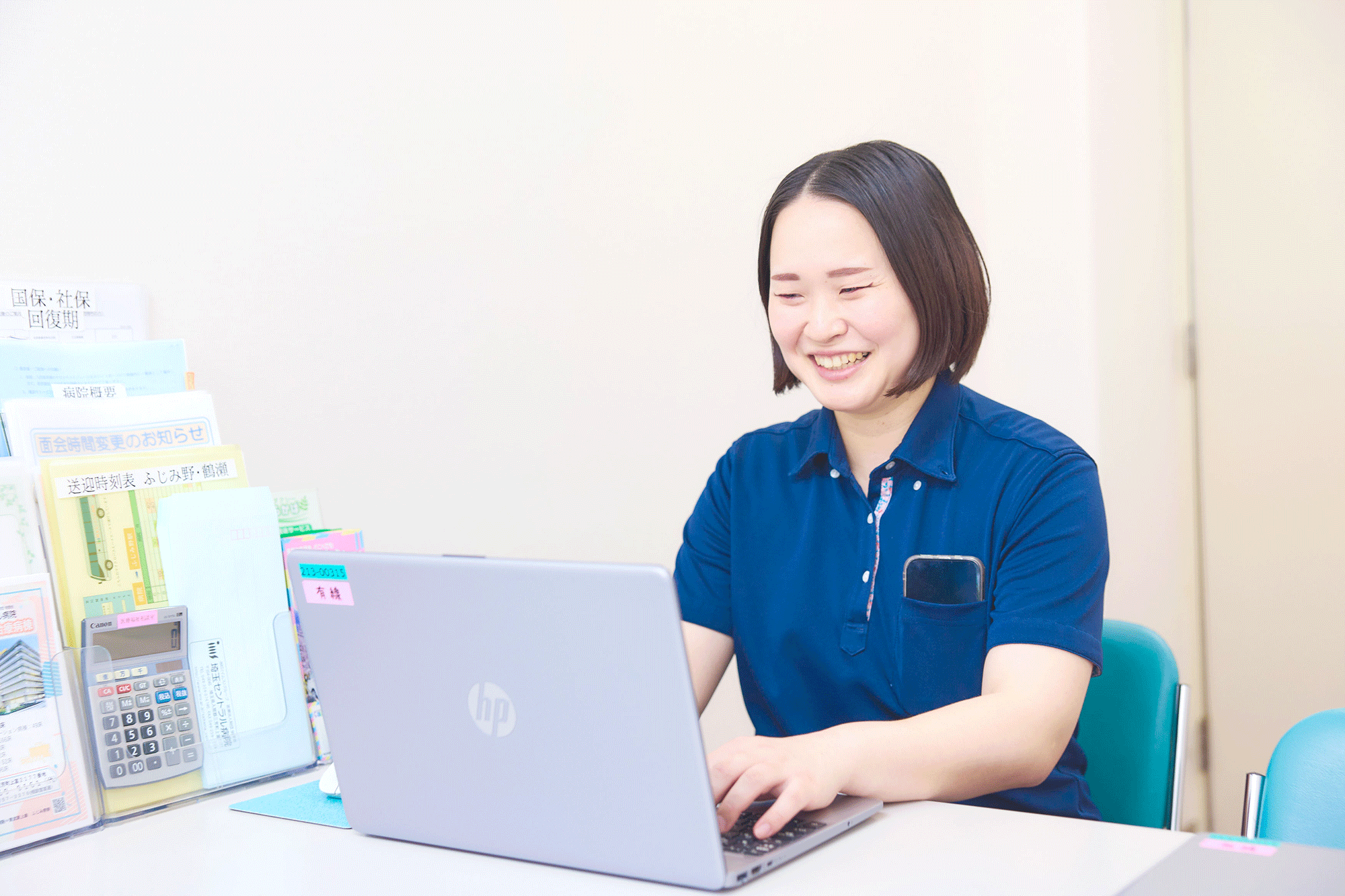 事務室でケアプランを作成する施設ケアマネジャーと電話対応するスタッフ
