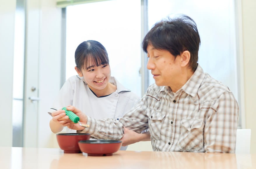 食事の介助を受けながら食べる練習に取り組む患者さまとスタッフ