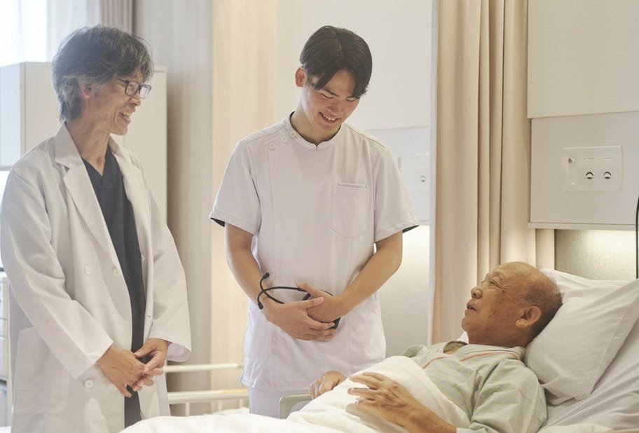 ベッドの高齢の患者さまに医師と看護師が笑顔で声をかける様子
