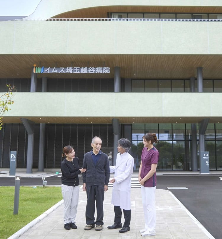 病院のエントランス前で笑顔で語らう患者さまと医師・看護師